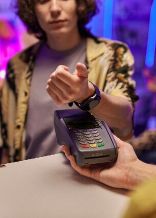 Eine Person hält die Smartwatch an ihrem Arm über ein Zahlungsgerät, das eine ihr hinhält.
