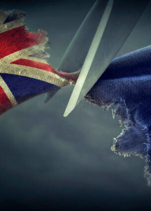 Eine Schere durchtrennt Stoff, auf dem die Flaggen von Großbritannien und der EU gedruckt sind.