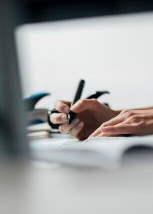 Aufnahme von zwei Händen, von denen eine einen Stift in der Hand hält und etwas auf einen Zettel schreiben will.