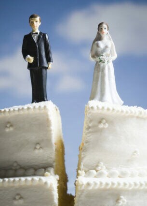 Figuren eines Bräutigams und einer Braut stehen auf einer Torte, die zwischen ihnen senkrecht geteilt wurde.