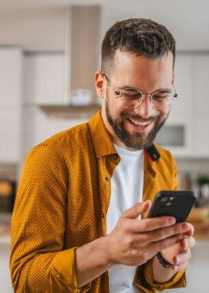 Eine Person hält ein Smartphone in den Händen und blickt lächelnd drauf.