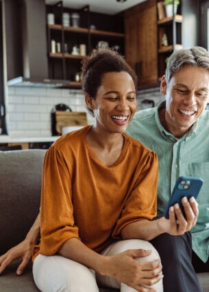 Zwei Personen sitzen gemeinsam auf einem Sofa und blicken zusammen auf ein Handy.