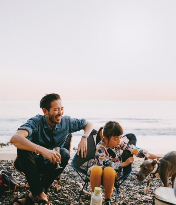 Father, daughter, and dog at campfire on beach.