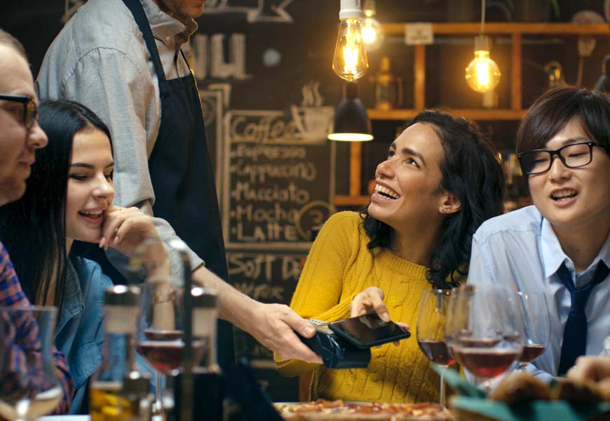 Woman paying with Tap to Pay at restaurant with friends